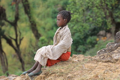 Side view of young woman sitting on rock