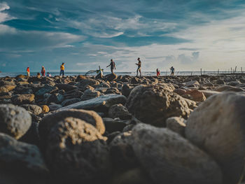 People on rocks at beach against sky