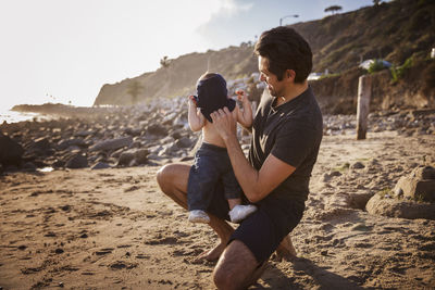 Happy father putting shirt to son at beach