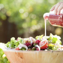 Cropped hand pouring dressing in bowl of salad