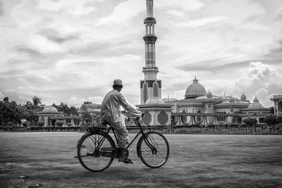 Man riding bicycle against sky in city