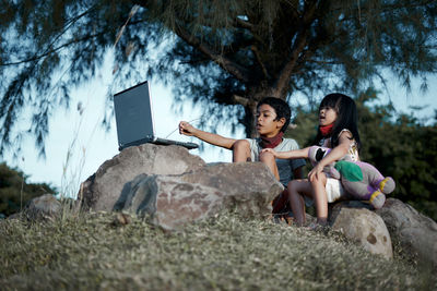 Friends sitting by plants against trees