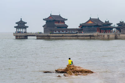 Rear view of man working in sea against building