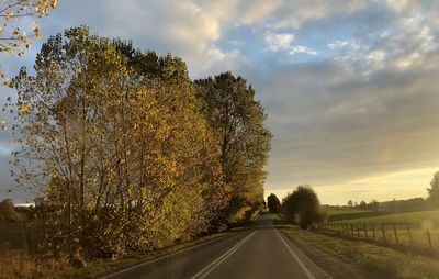 Road by trees against sky during sunset