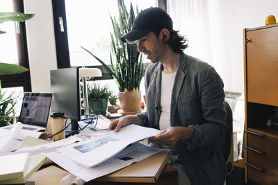 Male architect analyzing blueprint while sitting at desk in home office