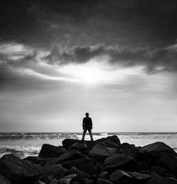 Man standing on rock at beach against sky