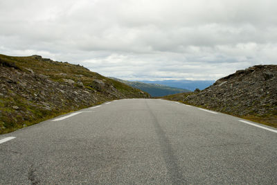 Empty road by mountains against sky