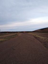 Dirt road passing through landscape against sky