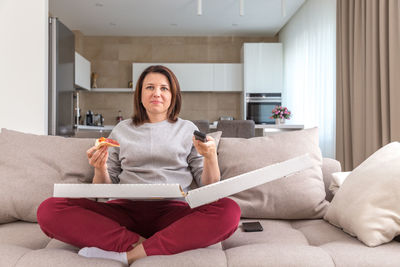 Woman eating pizza while sitting on sofa