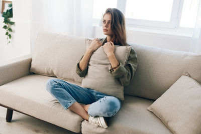 Young woman using phone while sitting on sofa at home