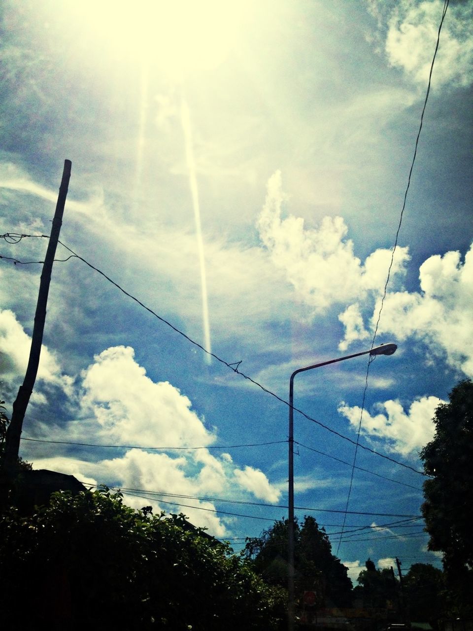 low angle view, power line, electricity, connection, sky, electricity pylon, power supply, cable, cloud - sky, fuel and power generation, sun, sunbeam, technology, tree, power cable, cloudy, sunlight, cloud, lens flare, day