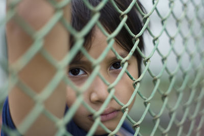 Portrait of boy seen through chainlink fence