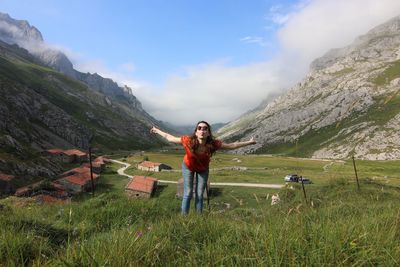 Full length of young woman standing on mountain against sky and mountains 