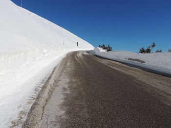 Road amidst snowcapped landscape against clear sky