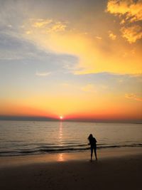 Silhouette woman standing on beach against sky during sunset