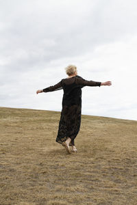 Rear view of woman with arms raised on field against sky