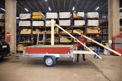 Salesman and male customer loading planks in trailer at hardware store