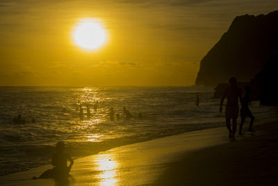 Silhouette people on beach against sky during sunset
