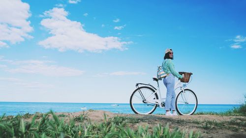 Woman with bicycle by sea against blue sky