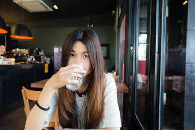 Portrait of young woman drinking glass at restaurant