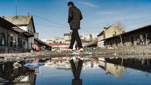 Reflection of man standing on puddle against buildings