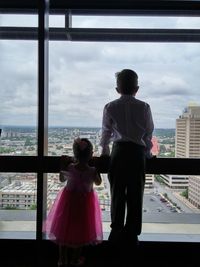 Rear view of siblings looking city through window