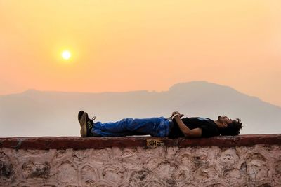 Man sleeping on sofa against orange sky