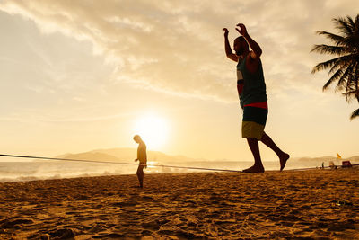 Man slacklining at beach against sky during sunset