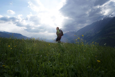 Side view of female hiker walking on field against cloudy sky