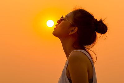 Optical illusion of woman reaching sun against clear sky during sunset