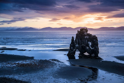 Rock formation on beach against sky during sunset