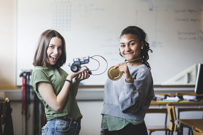 Portrait of successful female teenage students holding robot and gold medal while standing in classroom at high school