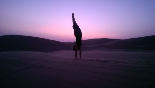 Silhouette man handstand on sand against sky during sunset