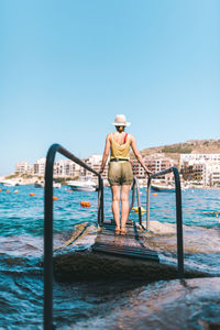 Rear view of man standing by sea against clear sky