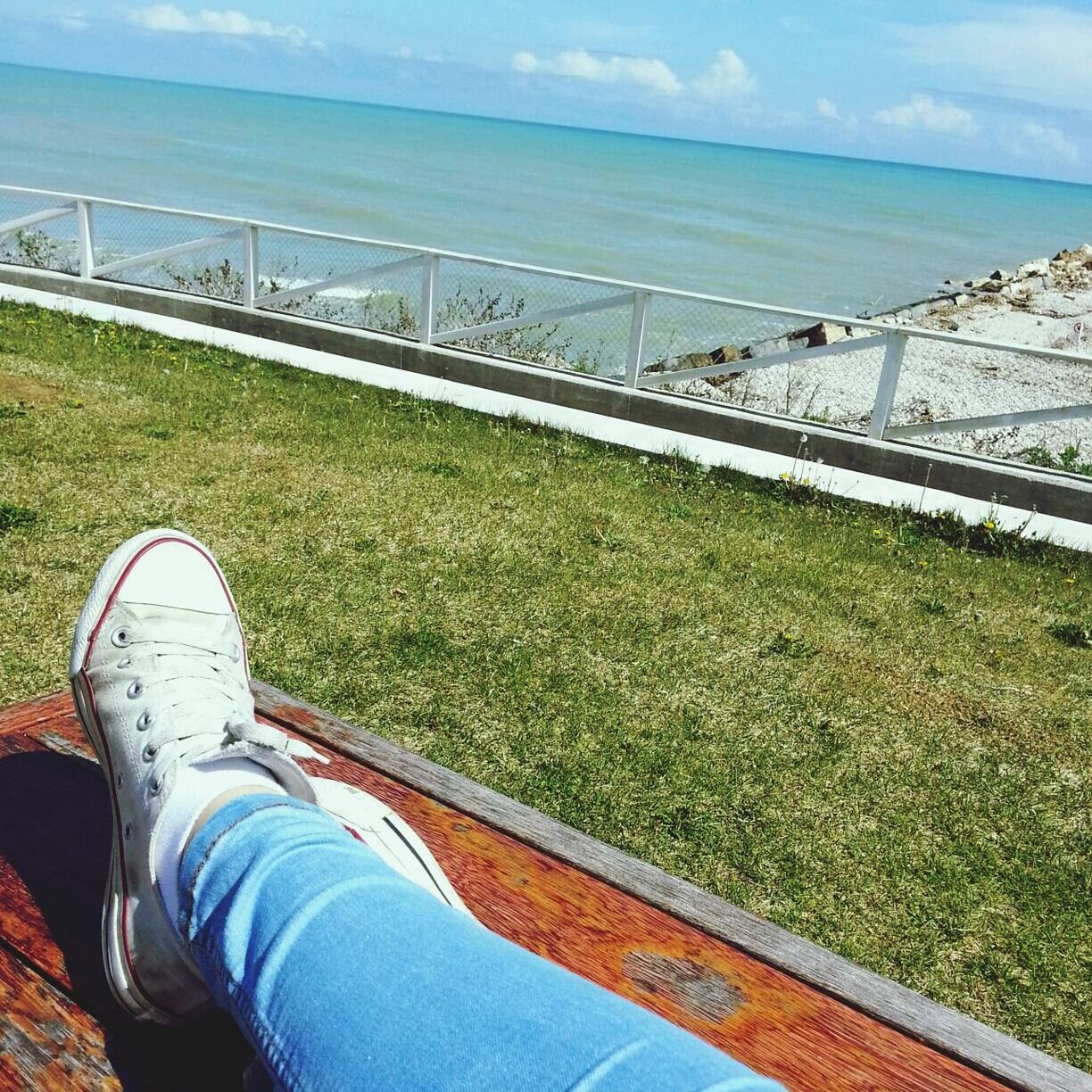 sea, low section, person, water, grass, sky, beach, personal perspective, horizon over water, tranquil scene, relaxation, leisure activity, tranquility, nature, lifestyles, scenics, shore, high angle view