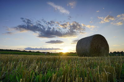 Hay bales on field against sky during sunset