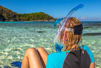 Woman wearing snorkel relaxing at beach against sky