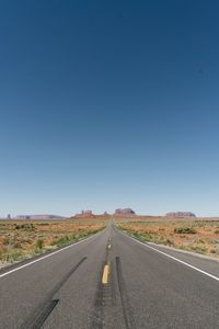 Road passing through landscape against clear blue sky