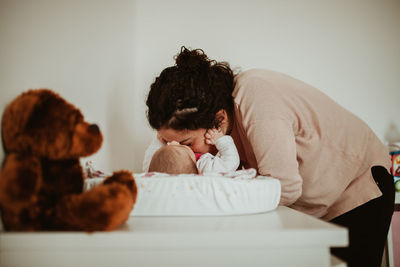 Woman kissing toddler daughter lying on table at home