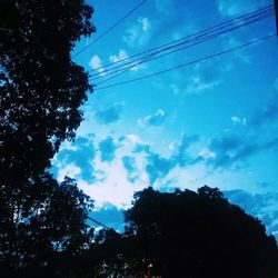 Low angle view of electricity pylon against cloudy sky