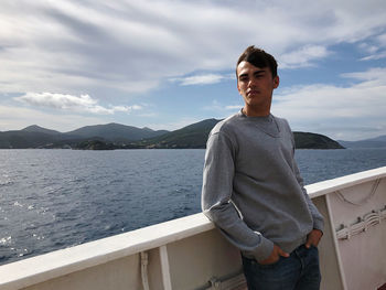 Young man standing on railing against sea