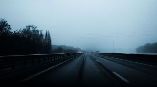 Road by trees against sky during foggy weather