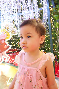 Portrait of charming 3 years old asian little girl with pink dress standing on lighting background.