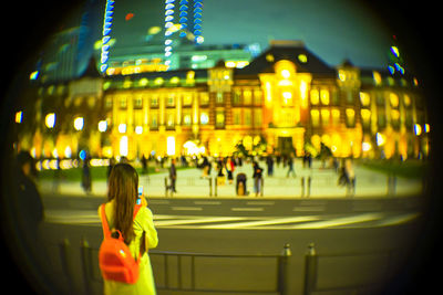 Rear view of people standing on illuminated street at night