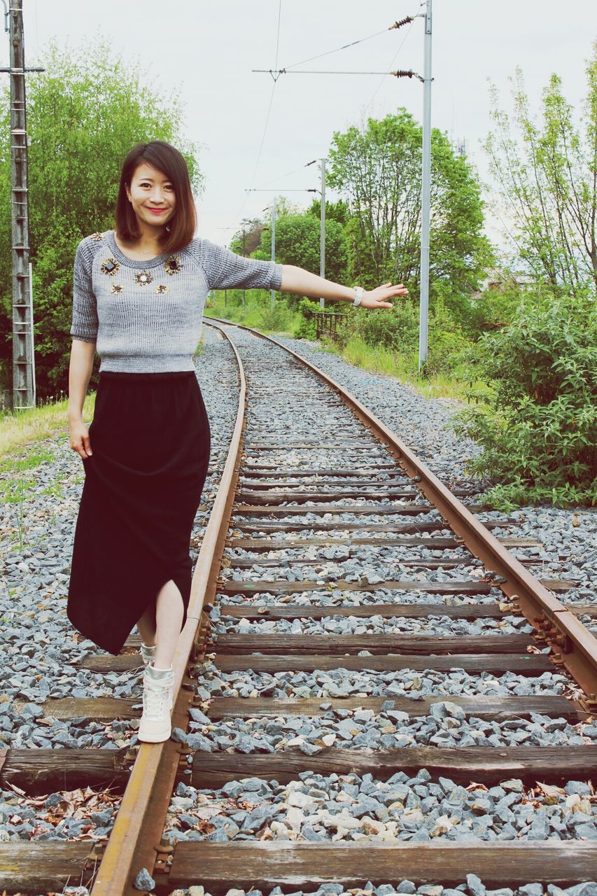 full length, casual clothing, railroad track, person, looking at camera, standing, portrait, lifestyles, tree, front view, railing, leisure activity, day, outdoors, rail transportation, young adult, steps, the way forward
