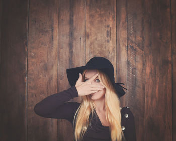 Portrait of woman hiding face with hand against wooden wall