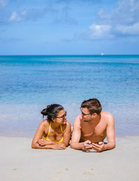 Rear view of woman relaxing at beach against sky