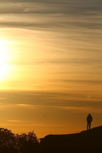 Silhouette man standing on landscape against sky during sunset