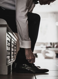 Low section of man tying shoelace while sitting on seat at home