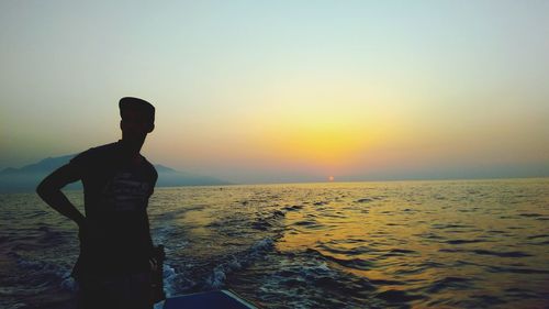 Rear view of silhouette man standing at beach against sky during sunset